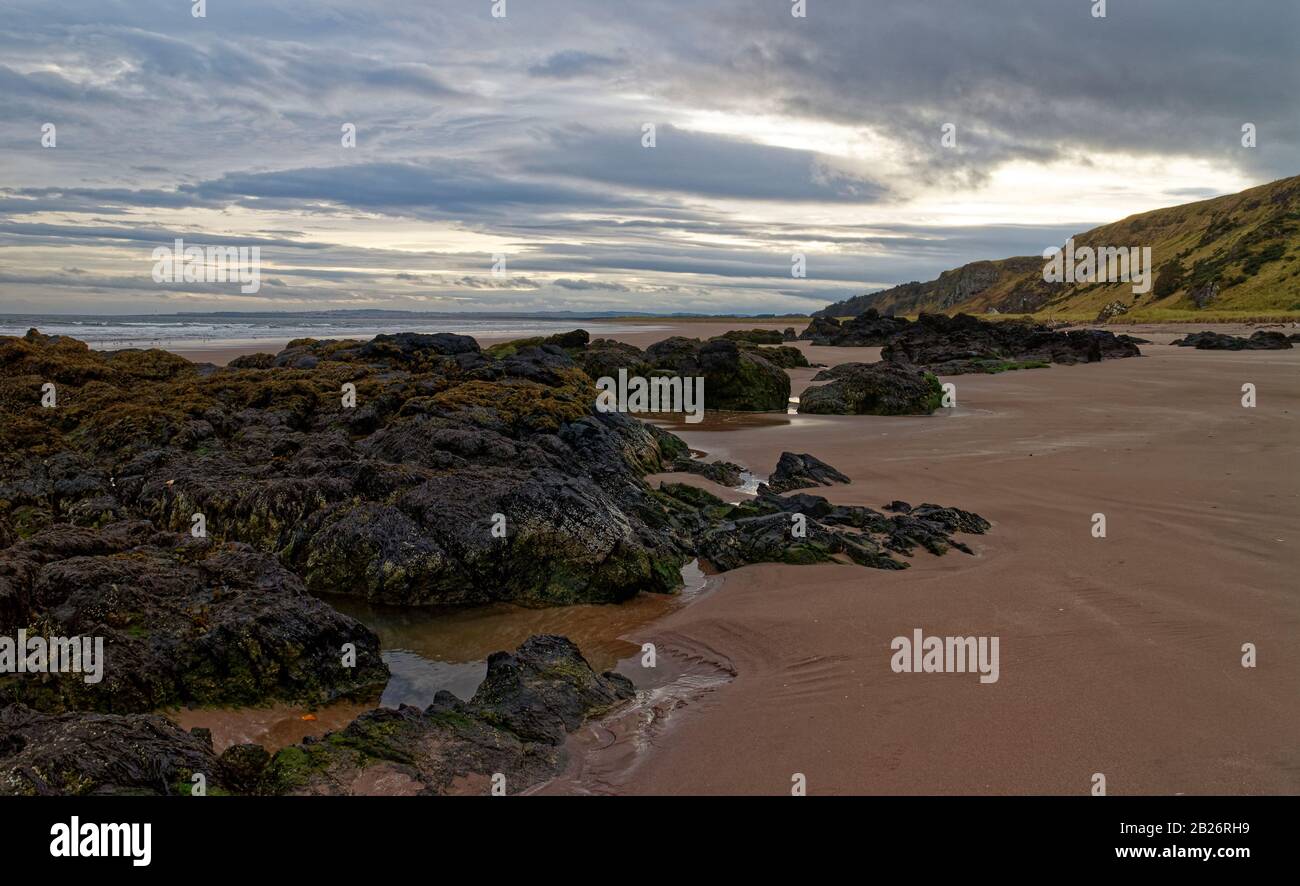 Volcanic Rocks and Rock Pools uncovered by the retreating tide on St Cyrus Beach on the East Coast of Scotland. Stock Photo