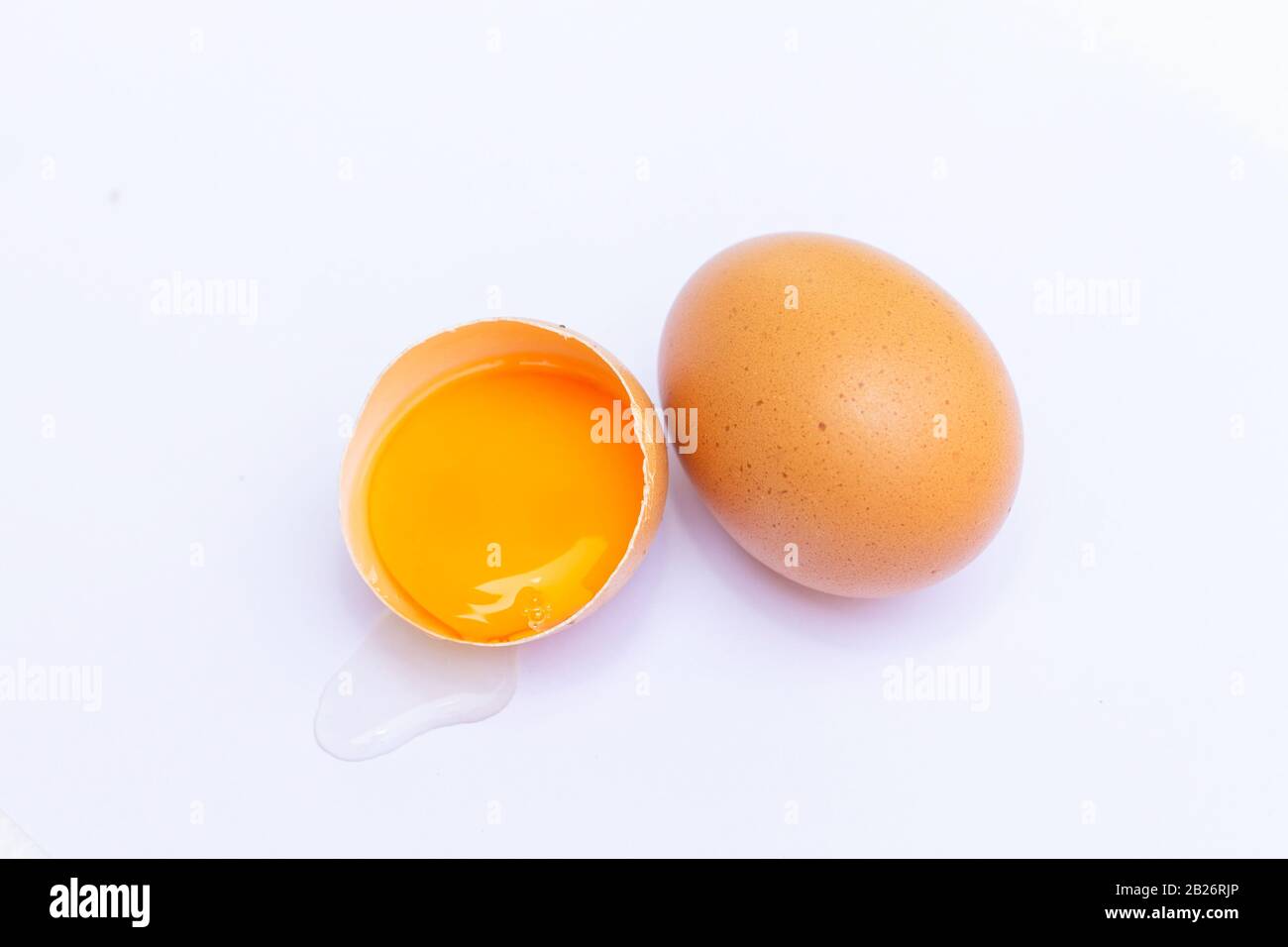 Two brown eggs With one egg broken in half, with a yolk inside the eggshell, laid on a white background Stock Photo