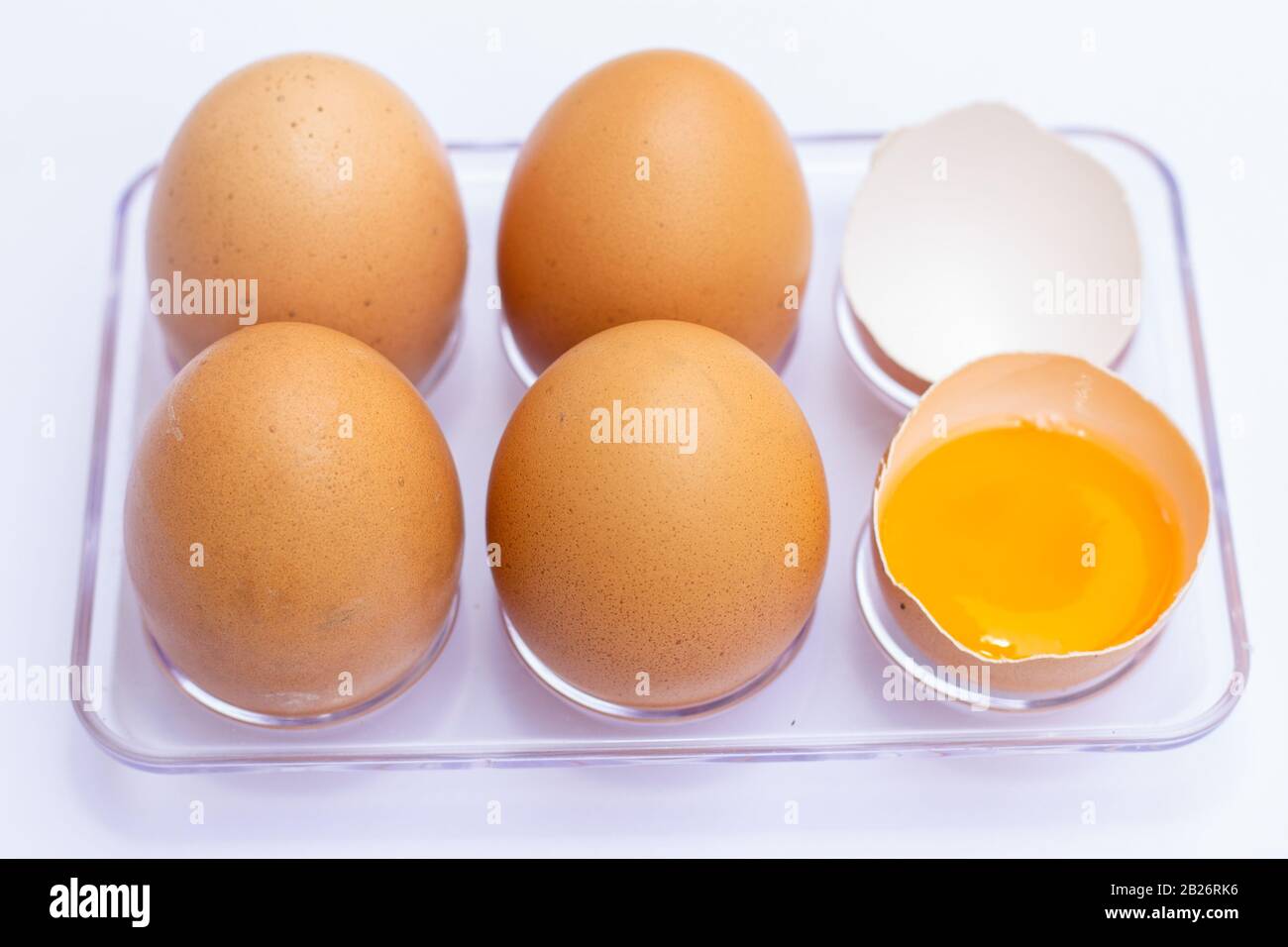 Four brown eggs lay on an egg tray with an eggshell on a white background. There was a broken egg, showing the yolk inside. Stock Photo