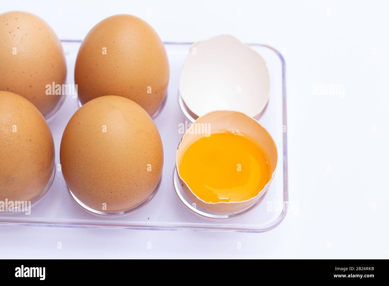Four brown eggs lay on an egg tray with an eggshell on a white background. There was a broken egg, showing the yolk inside. Stock Photo