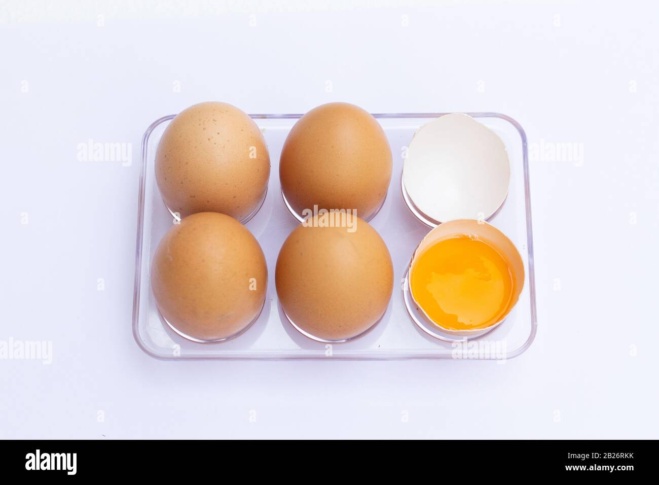 Four brown eggs lay on an egg tray with an eggshell on a white background. Stock Photo