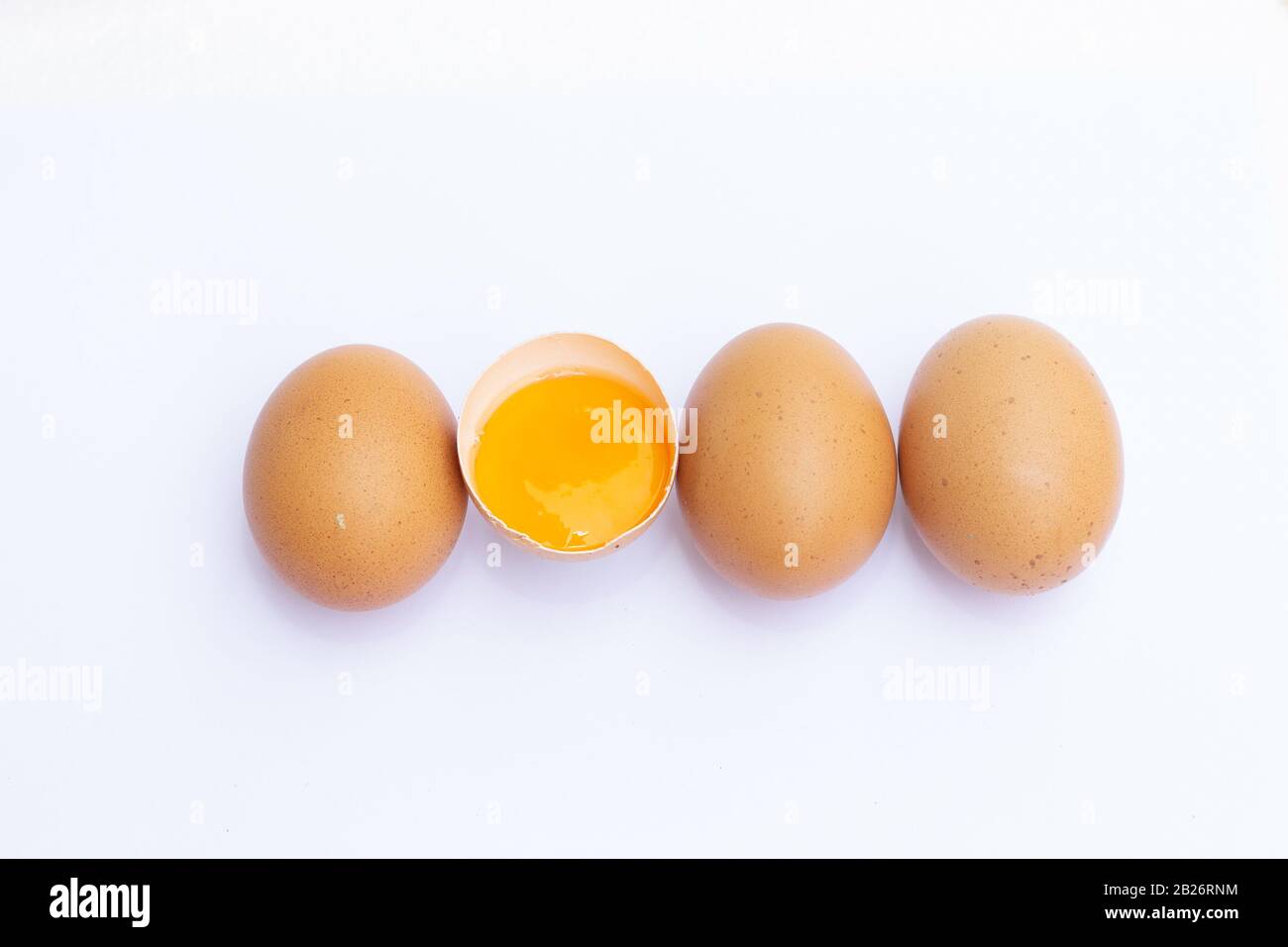 Four brown eggs arranged in a row on a white background And there was one egg broken in half, and saw the yolk in it. Stock Photo