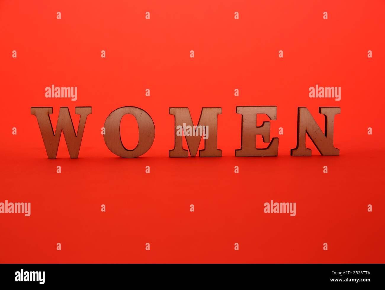 Word WOMEN made of decorative wooden letetrs standing in middle of intensive red color background, International Women's Day concept. Stock Photo