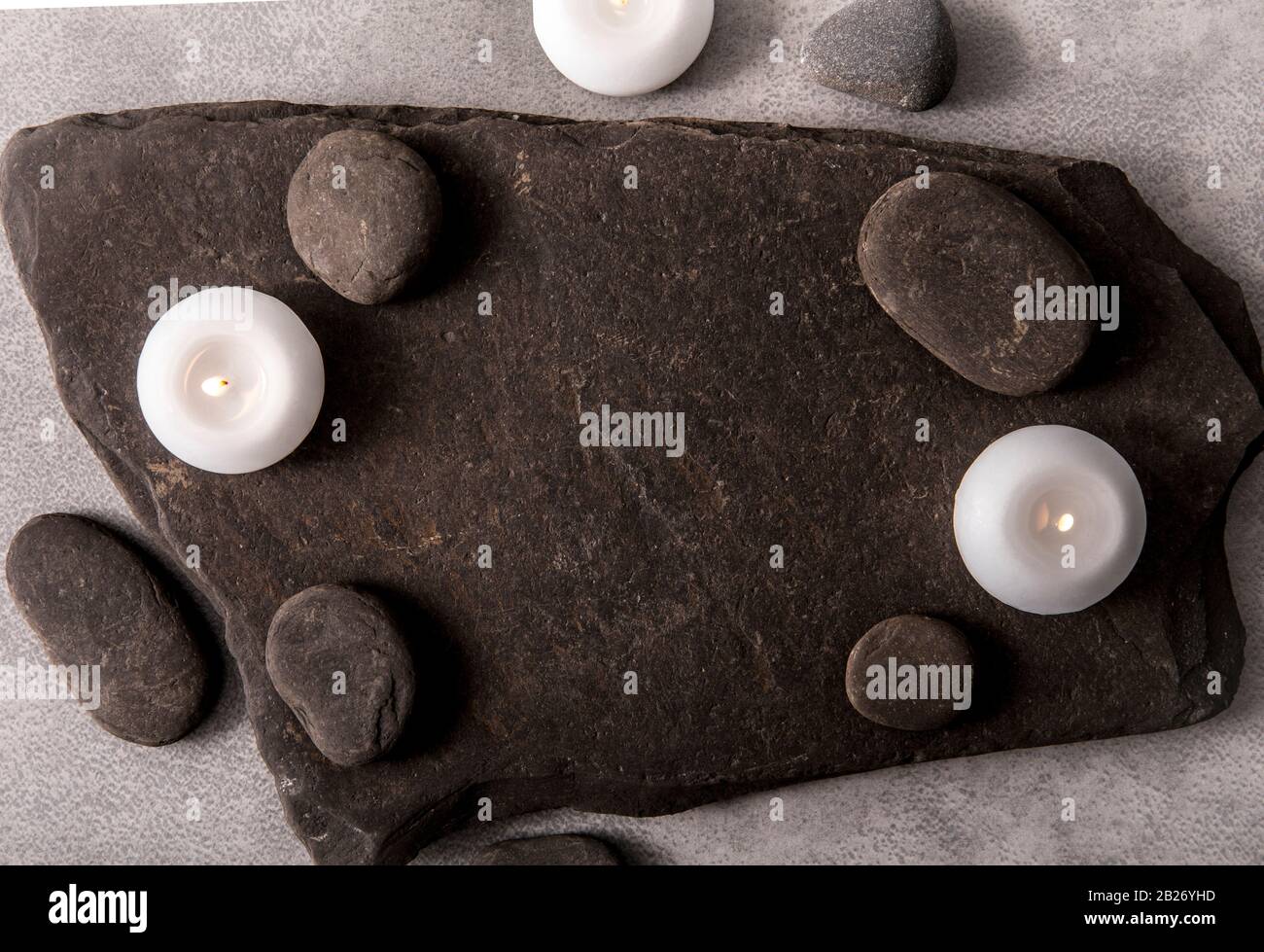 Frame made out of and black round smooth zen stones on black rough flat stone with white spa candles. Copy space. Stock Photo