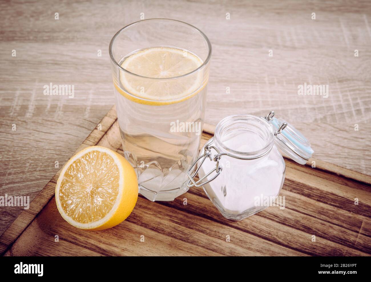 Baking soda in drinking glass with water and lemon juice, health benefits for digestive system concept on natural wooden background. Stock Photo