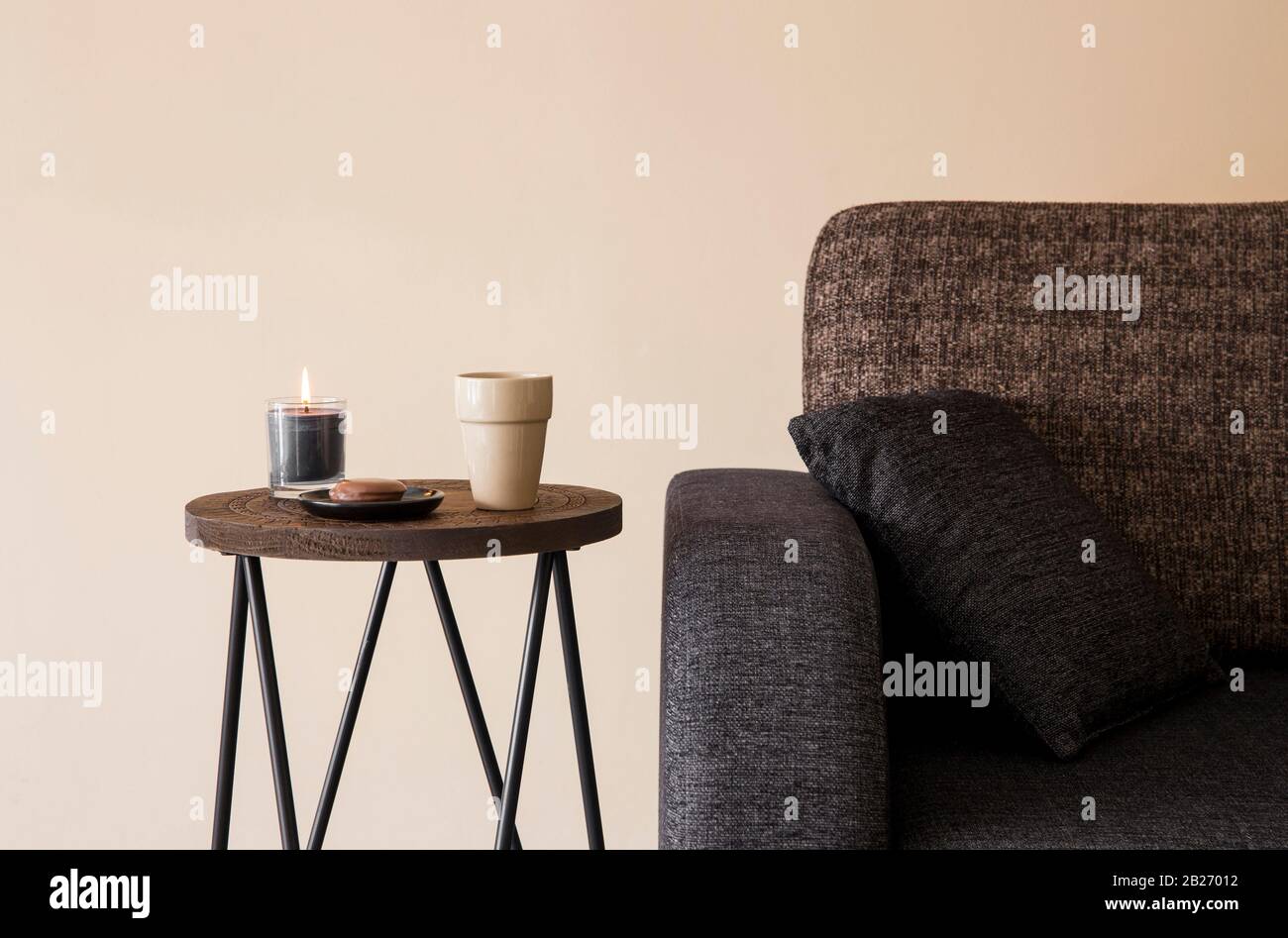 Detail view of modern round wood metal coffee table with cappuccino mug, glass candle burning by the side of sofa. Stock Photo