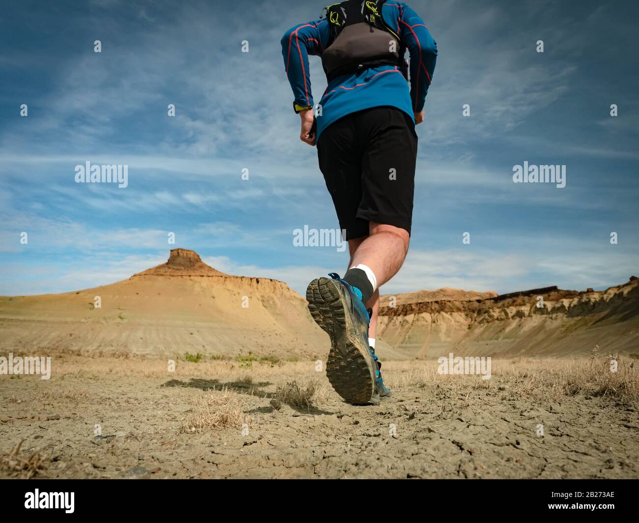 Runner athlete with backpack running on the wild trail at red mountains