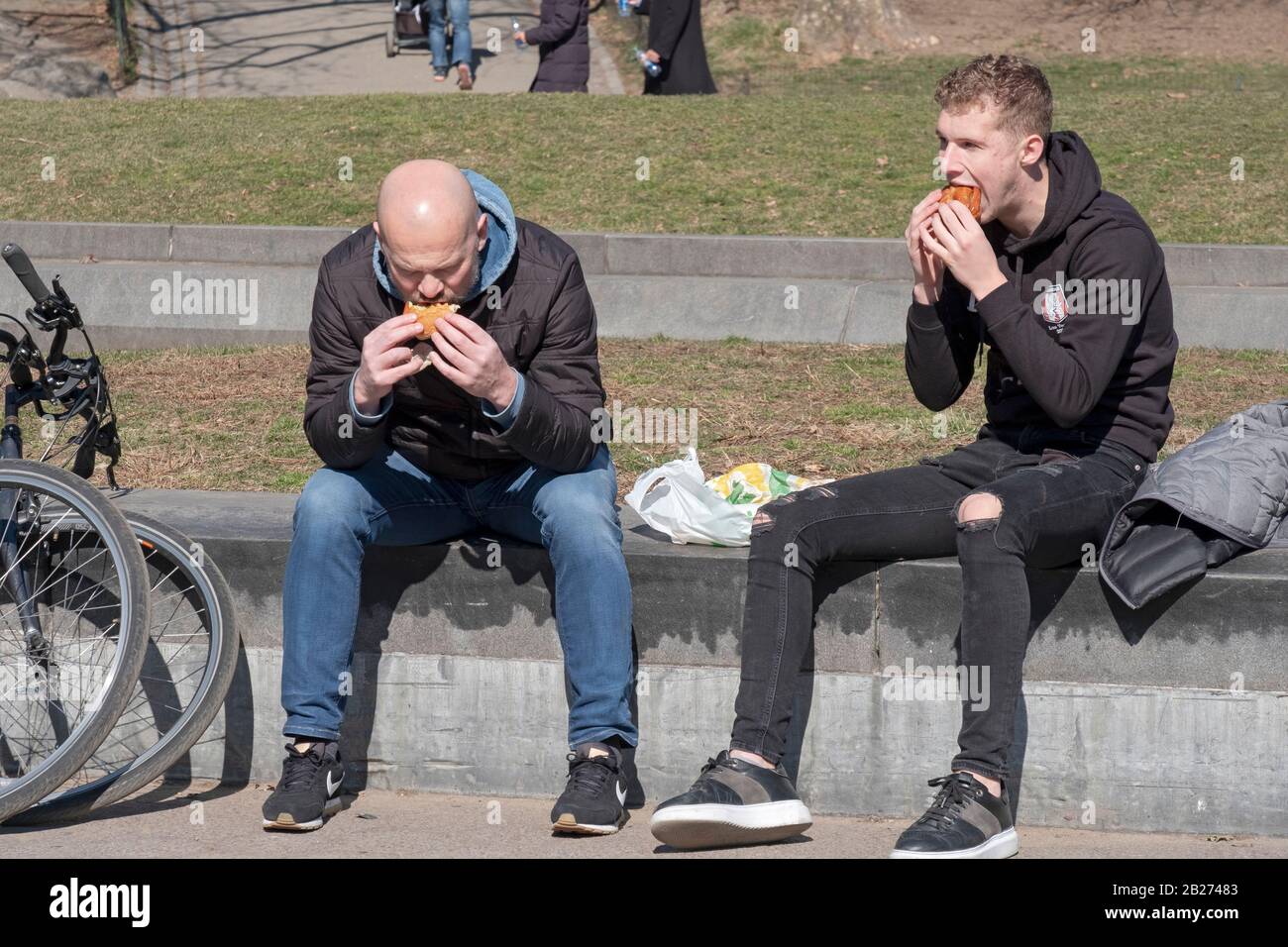 Two men, likely tourists, eat Subway's hero sandwiches in Central Park in Manhattan, New York City. Stock Photo