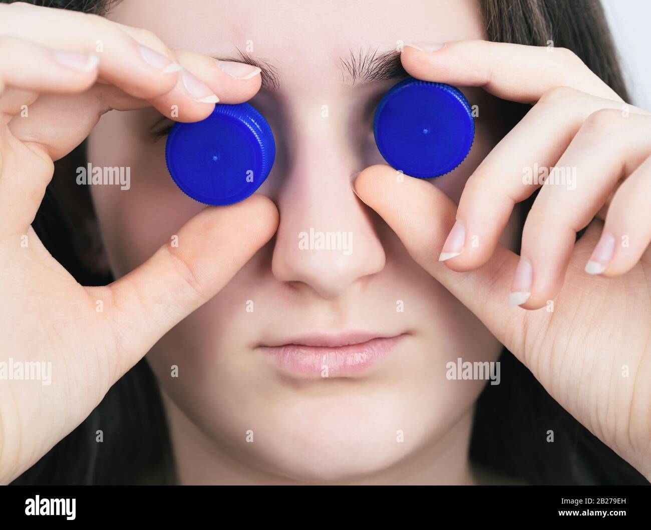 Portrait of a Brunette Teen Girl with Blue Plastic Bottle Caps Closeup Stock Photo
