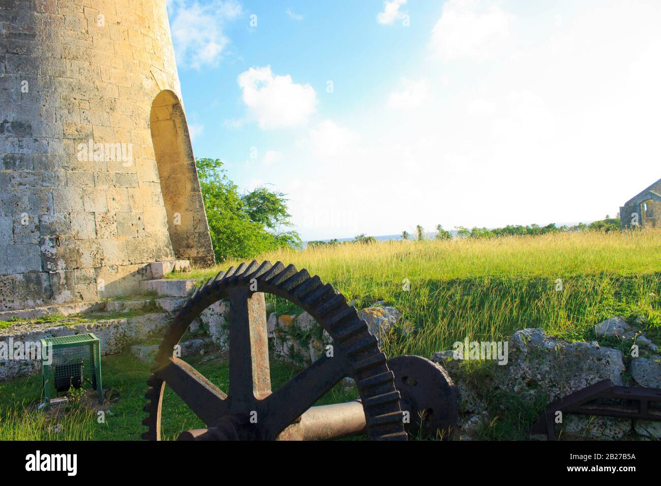 Breath-taking view of the ruin of an old mill and a mechanical part on a grassy ground with rocks at the golden hour with a bright blue sky Stock Photo