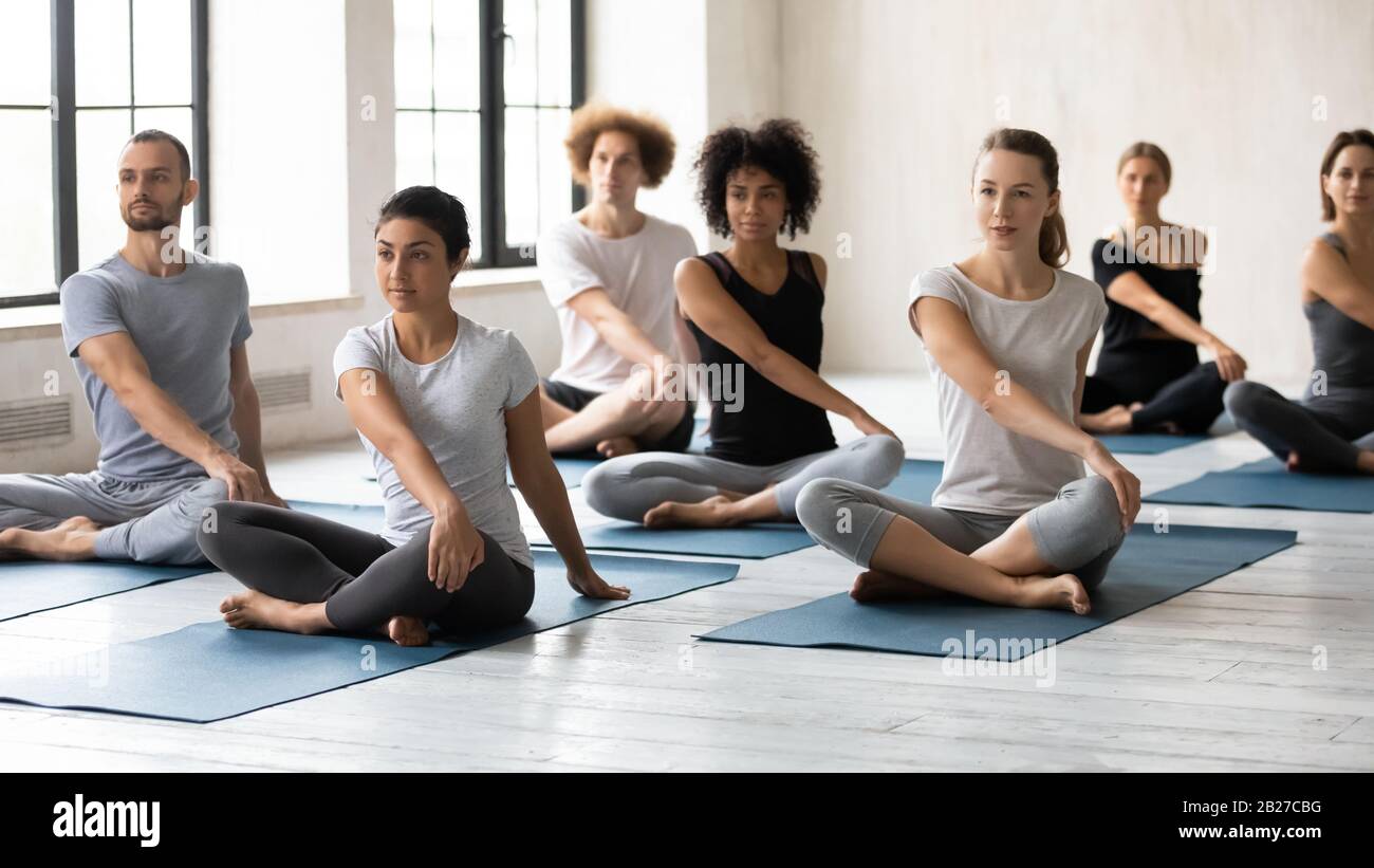 Seven diverse people during yoga class performing Easy Twist Pose Stock Photo