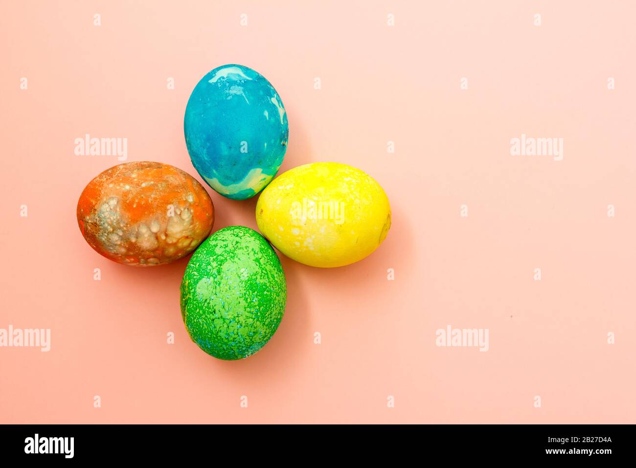 Four multi-colored Easter eggs on pink background top view, space for text. Concept happy easter day. Stock Photo