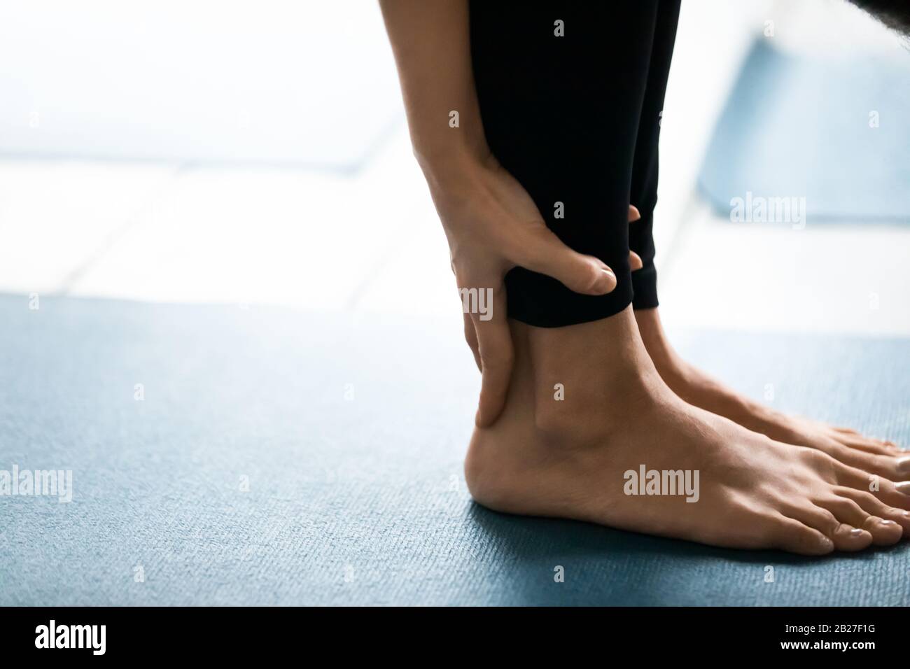 Closeup female legs standing barefoot on carpet performing Uttanasana