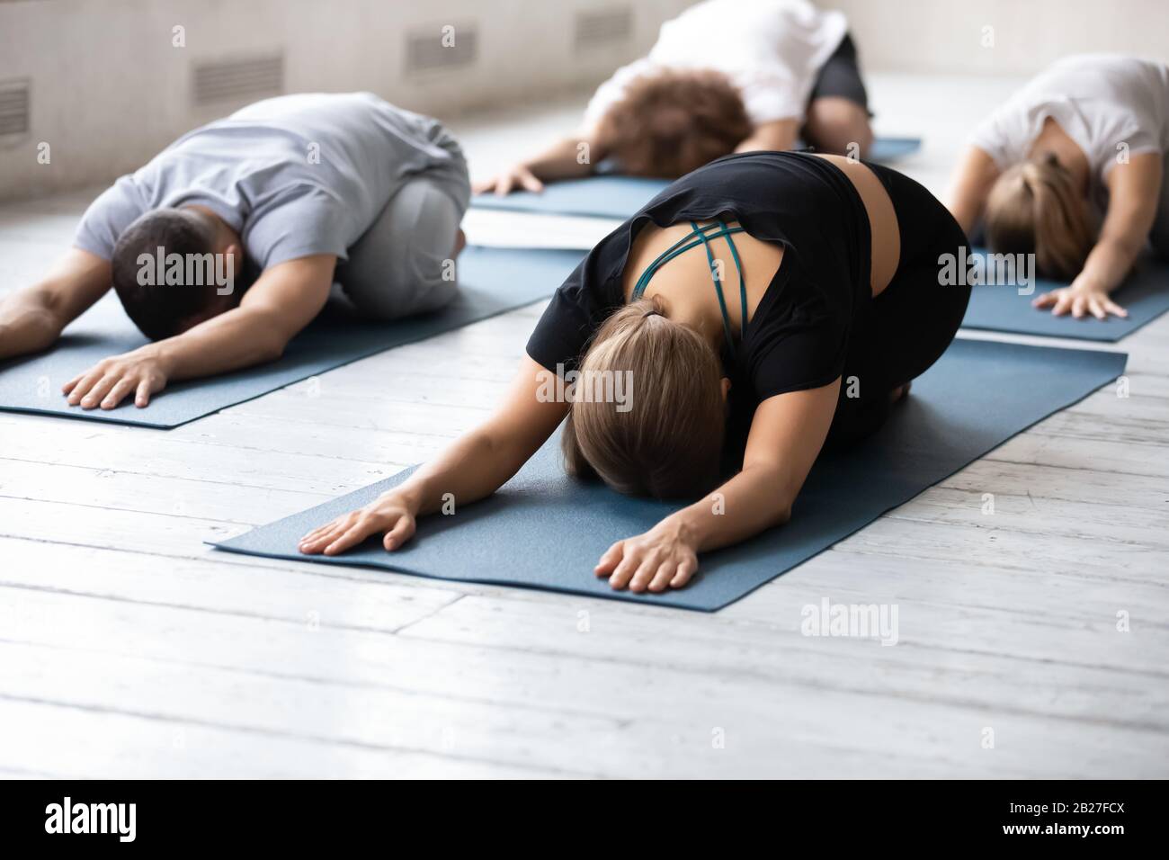 People in comfy activewear performing Balasana relaxation exercise during session Stock Photo