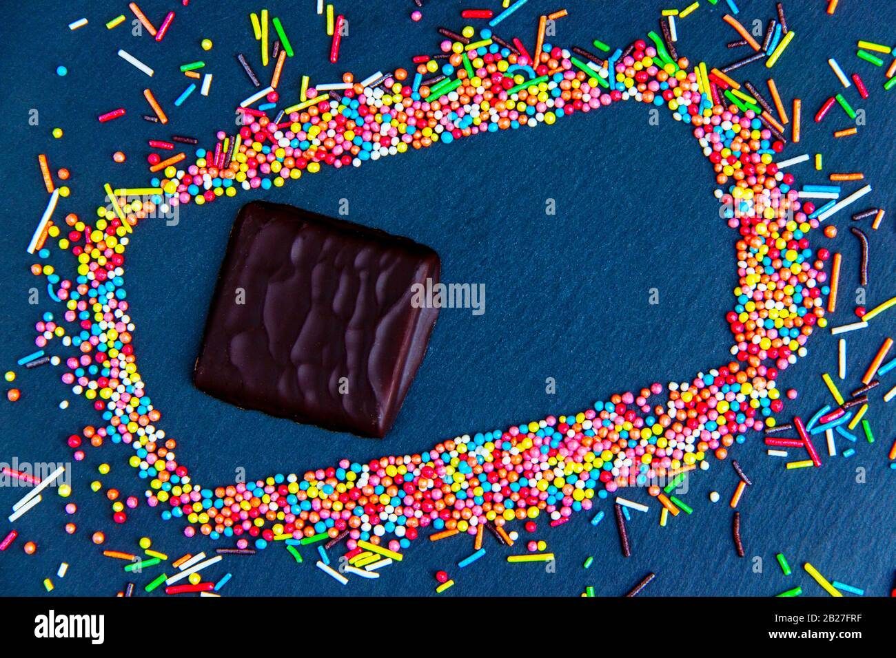 Easter greeting card with colorful candy frame and Easter egg, chocolate bunny and eggs. Top view on stone table with space for your greetings Stock Photo
