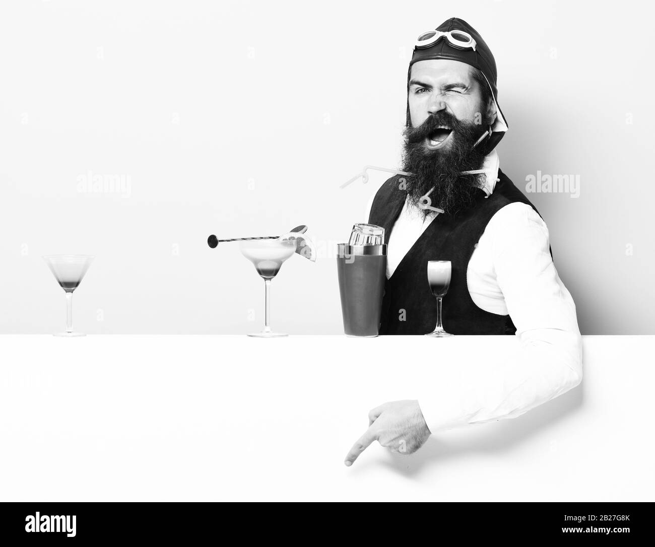 handsome bearded pilot with long beard and mustache on funny face with shaker alcoholic cocktail in vintage suede leather waistcoat with hand, and glasses on purple green studio background Stock Photo