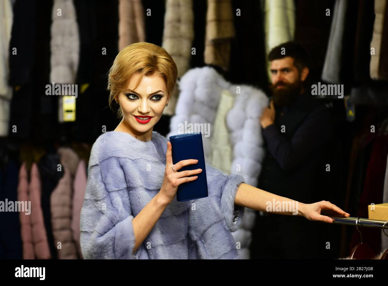 Lady tries expensive mink overcoats on. Seller with beard and woman
