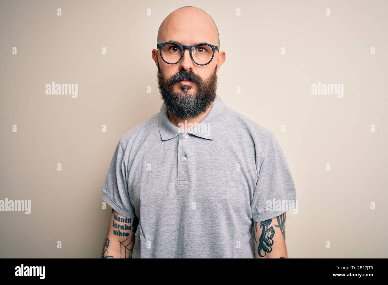 Handsome bald man with beard and tattoo wearing casual polo and glasses  with serious expression on face. Simple and natural looking at the camera  Stock Photo - Alamy