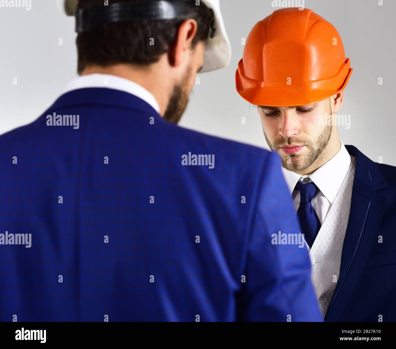 Construction, business people, architecture concept. Engineers with serious faces. People in helmets isolated on white background. Architects think about project. Businessman and engineer back view. Stock Photo