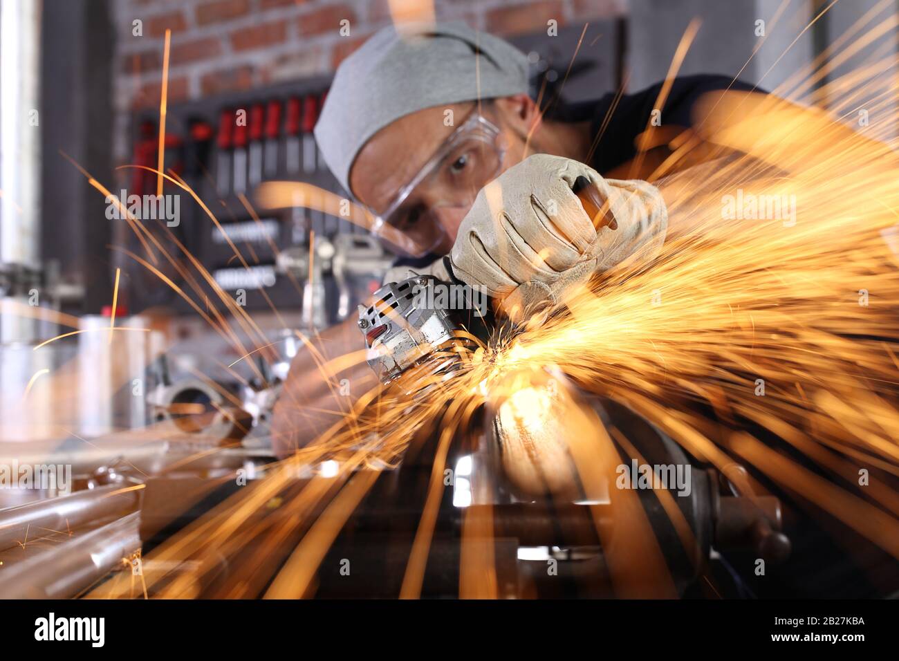 man work in home workshop garage with angle grinder, goggles and construction gloves, sanding metal makes sparks closeup, diy and craft concept Stock Photo