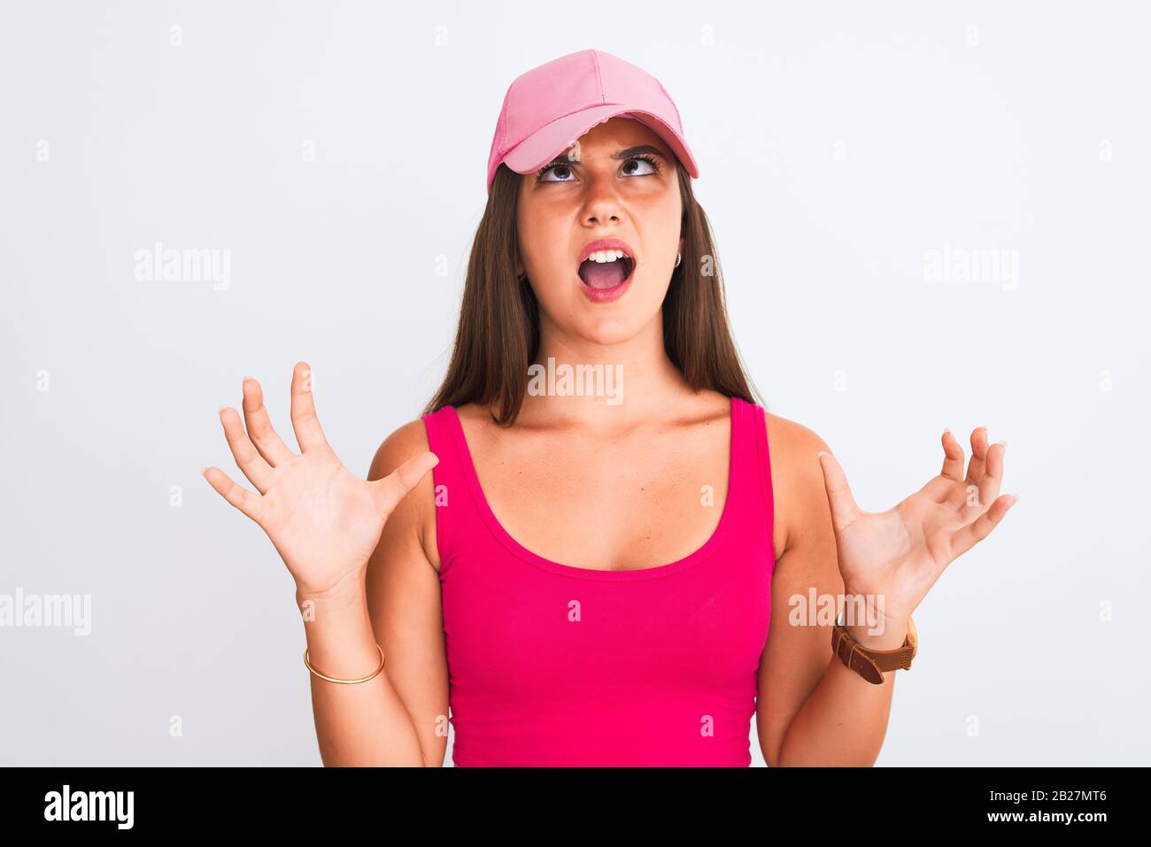 Young beautiful girl wearing pink casual t-shirt and cap over isolated white background crazy and mad shouting and yelling with aggressive expression Stock Photo