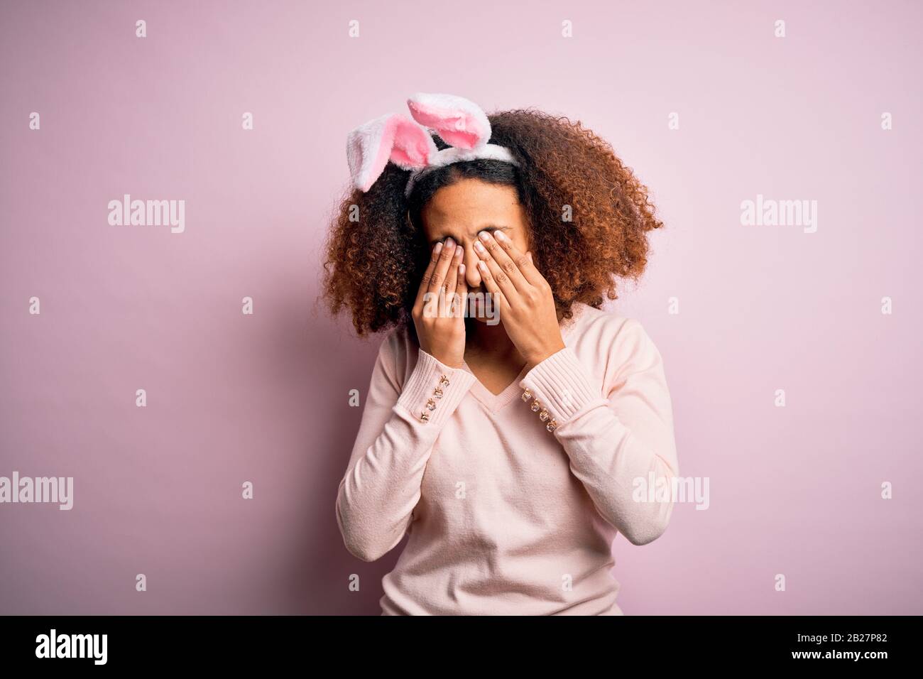 Young african american woman with afro hair wearing bunny ears over pink background rubbing eyes for fatigue and headache, sleepy and tired expression Stock Photo