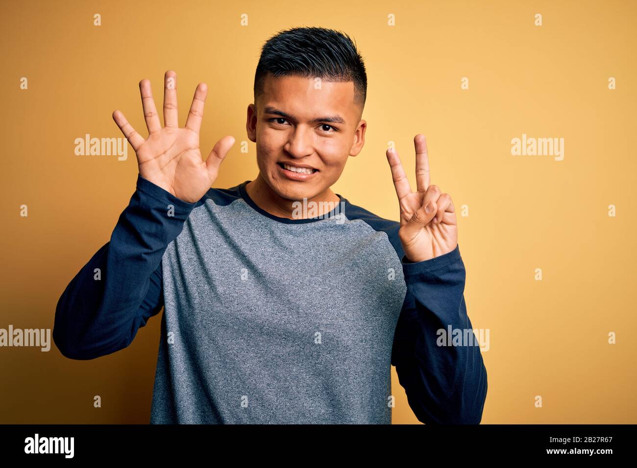 Young handsome latin man wearing casual t-shirt standing over yellow