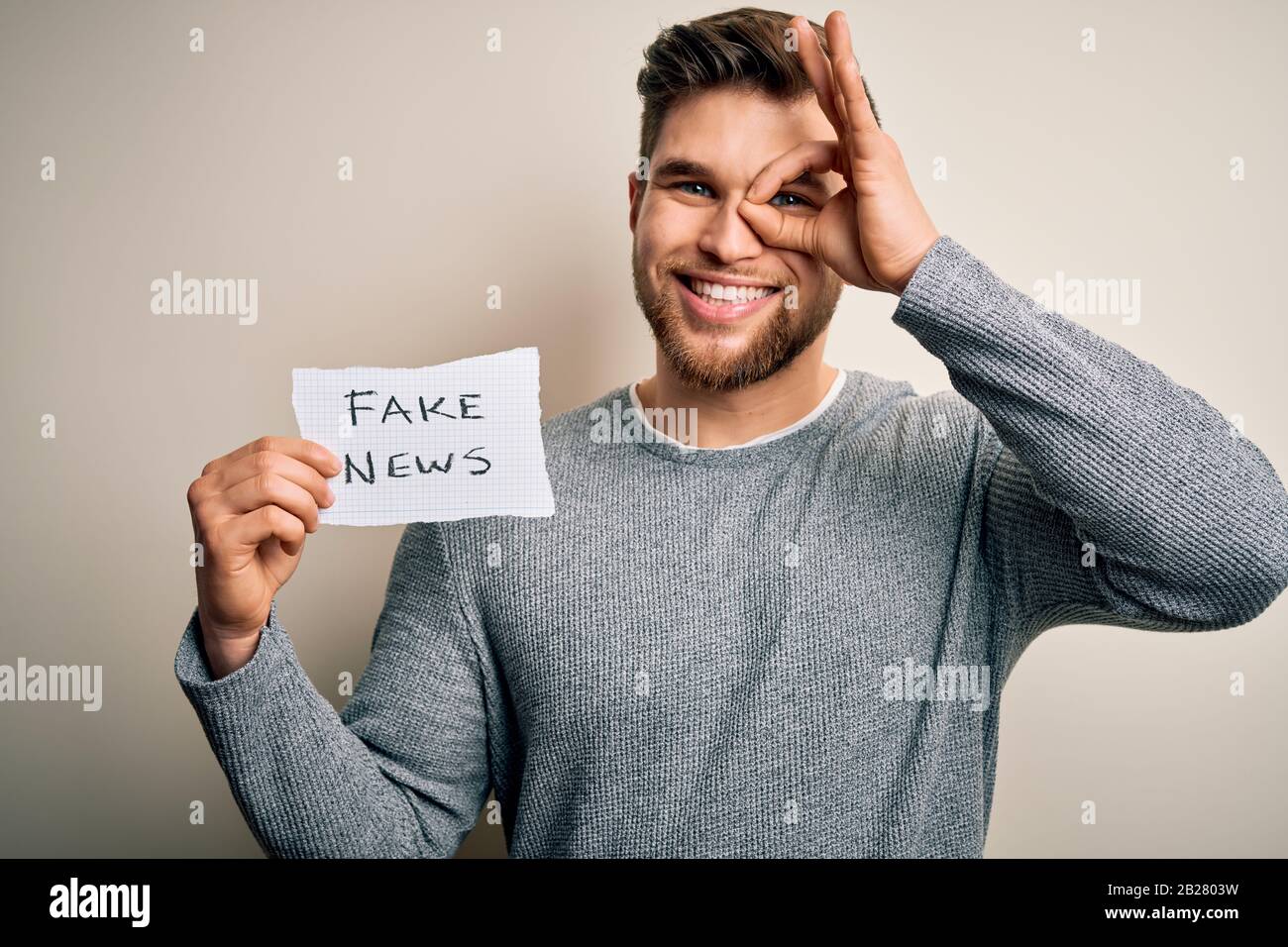 Young blond man with beard and blue eyes holding paper with fake news ...