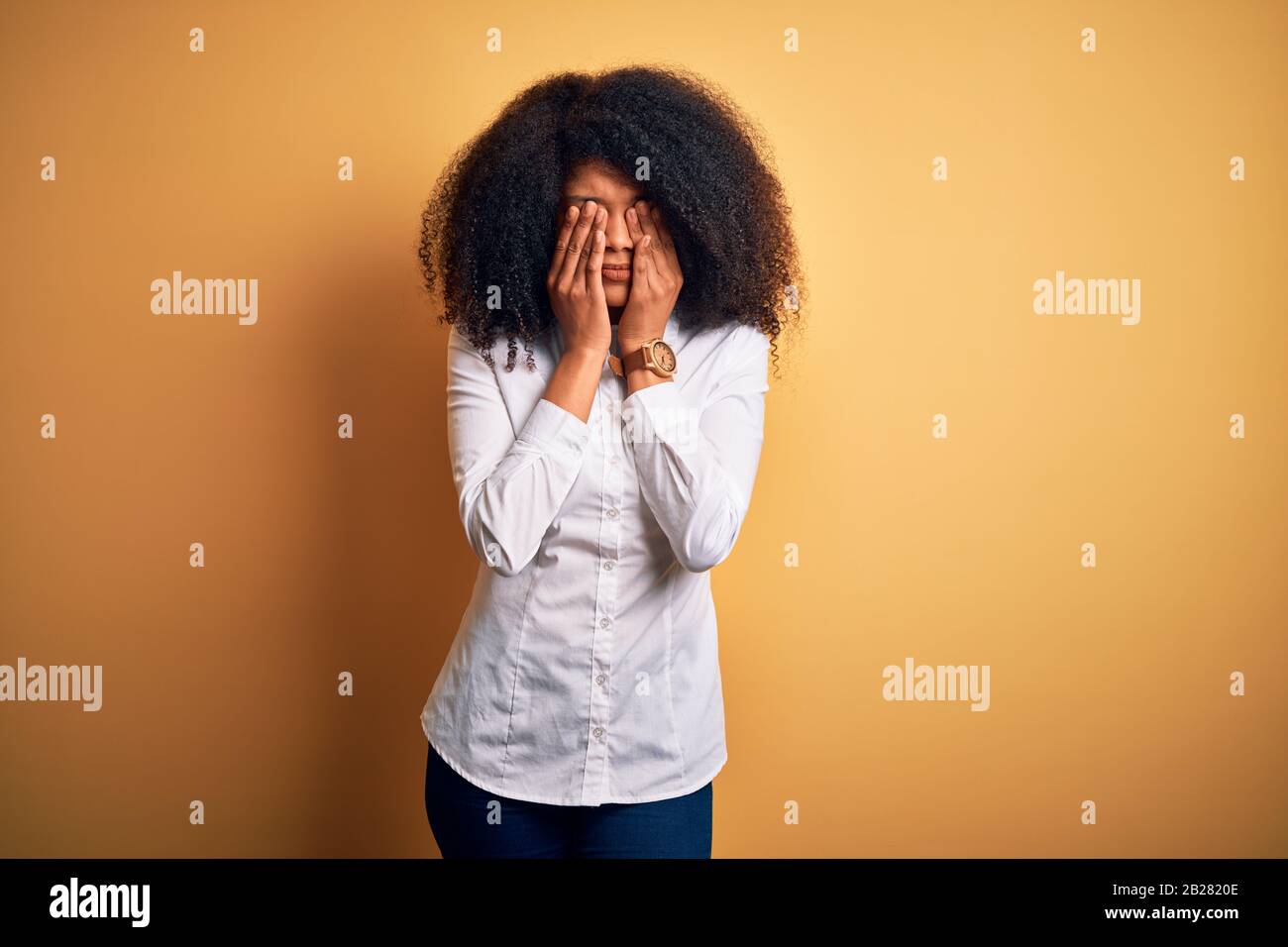 Young beautiful african american elegant woman with afro hair standing over yellow background rubbing eyes for fatigue and headache, sleepy and tired Stock Photo
