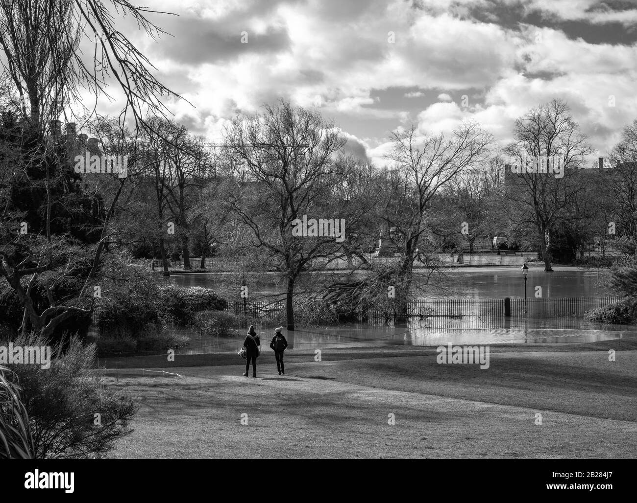 Winter in public gardens in York.  A path stretches down towards a flooded river with a broken tree and two young people look on. Stock Photo