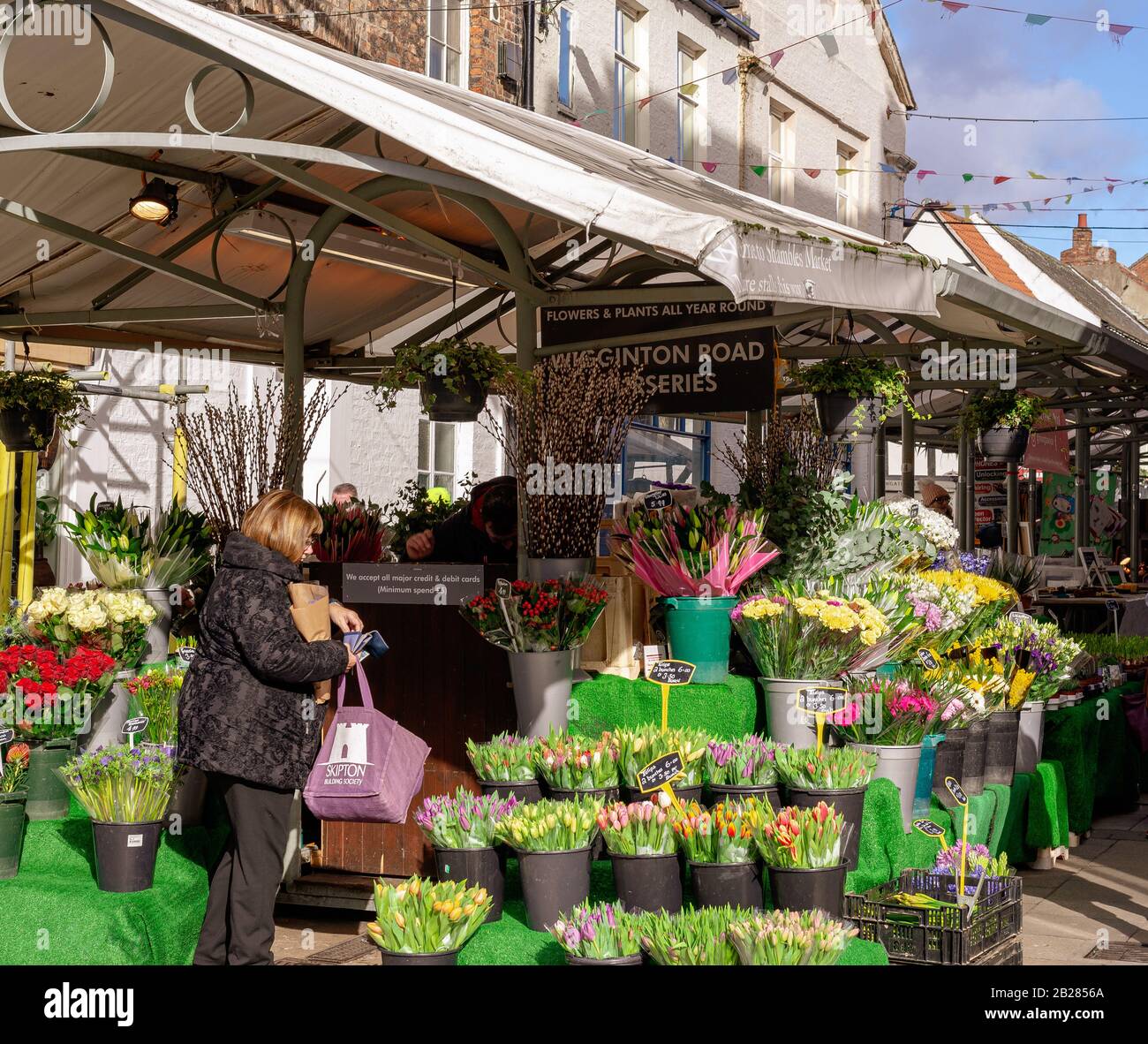 York Market during a winter afternoon.  A woman shops at flower stall caught in the winter sun. People pass by. Stock Photo