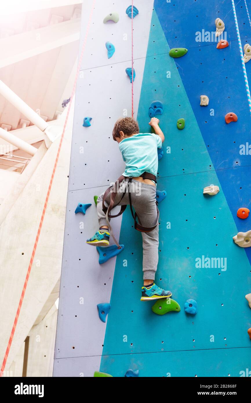 Boy climb on the rock climbing wall griping with hands view from bellow ...