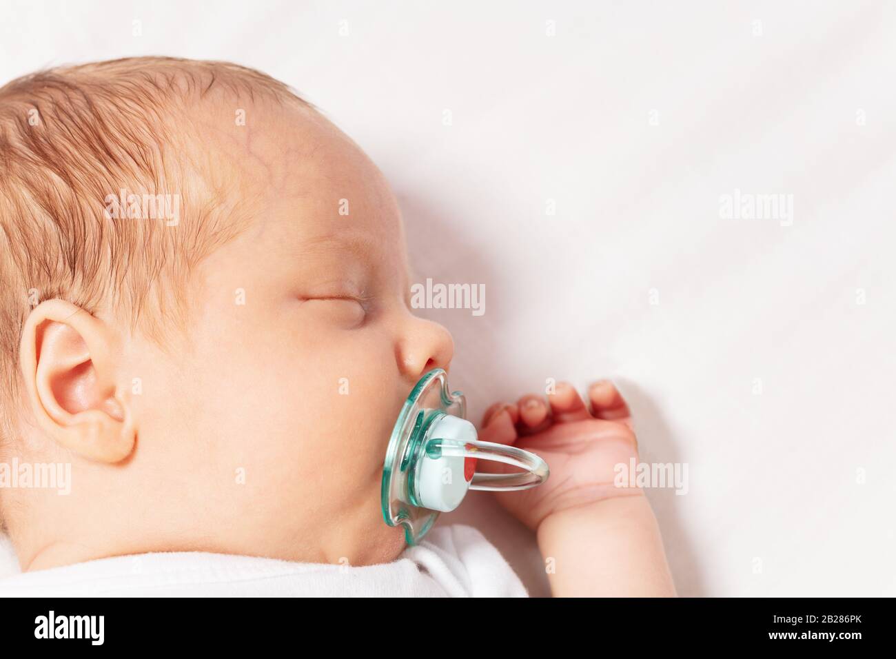 Face closeup portrait of newborn infant baby boy laying on the bed with pacifier sleeping Stock