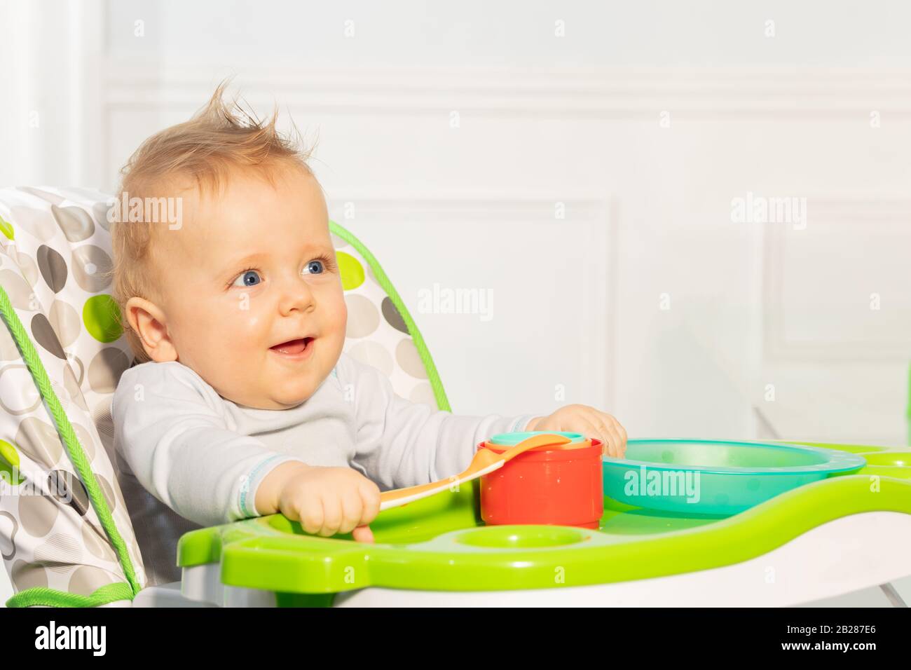 Happy little toddler baby boy sit in highchair holding plastic spoon
