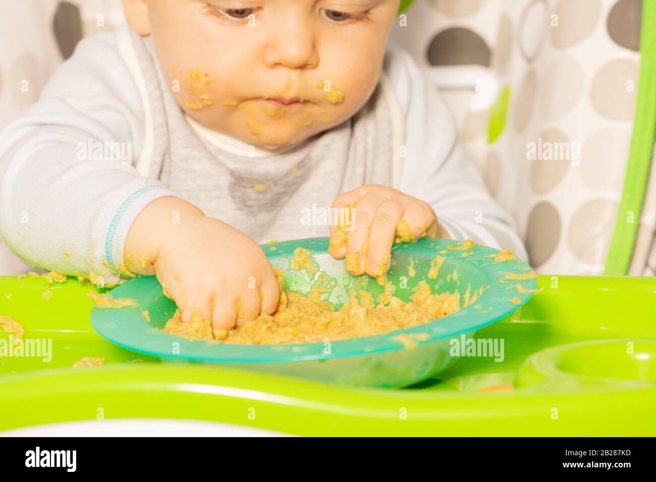 Toddler boy sit in high chair and play putting hands in plastic plate