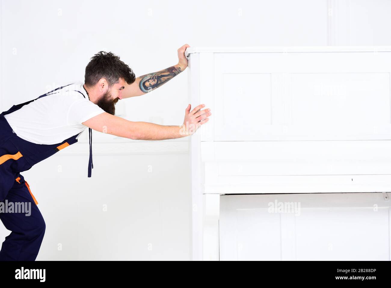 Man with beard and mustache, worker in overalls pushes piano ...