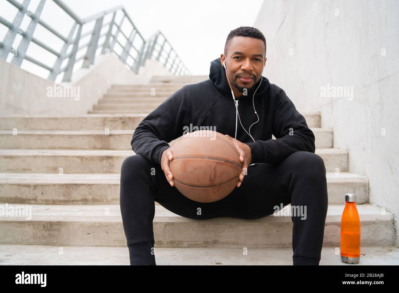 Portrait of an athletic man holding a basket ball while sitting on concrete stairs. Sport concept. Stock Photo