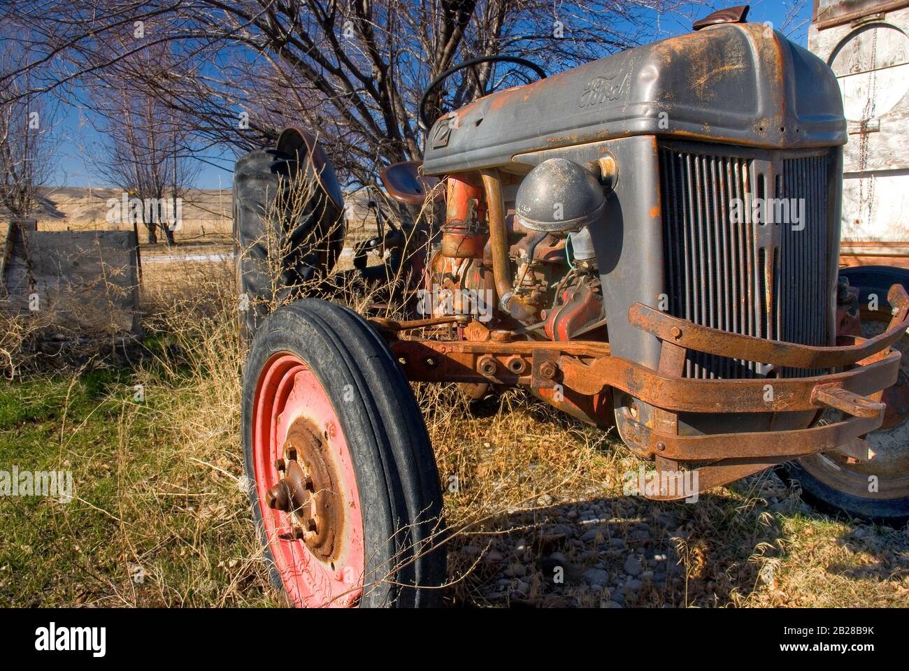 Old, Broken, Rusty For Tractor sits idle in the weeds on a Sunny Day Stock Photo