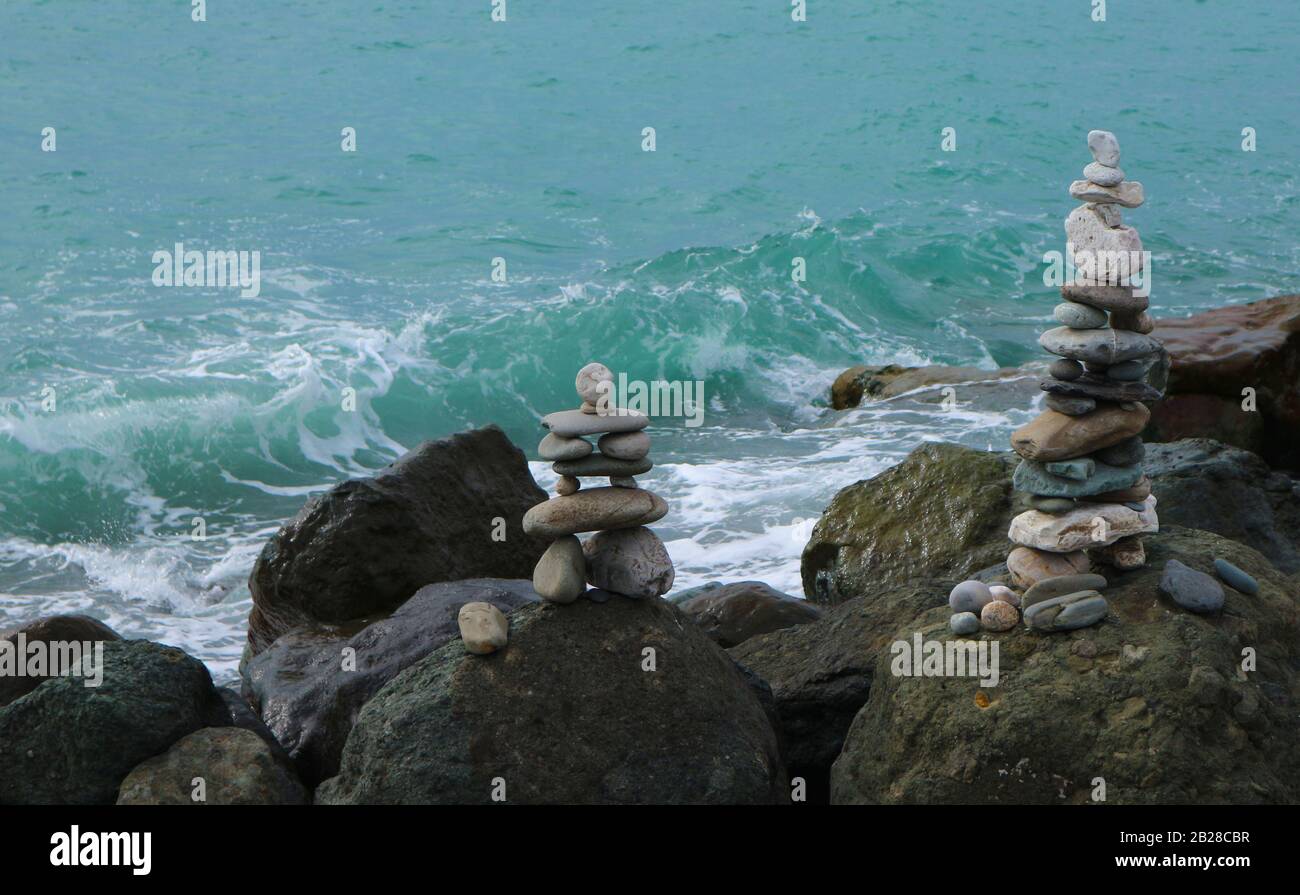 Stone cairn on seacoast in front of wave. Big rocks and balanced pebbles stack. Relaxation, harmony, balance concept. Stock Photo