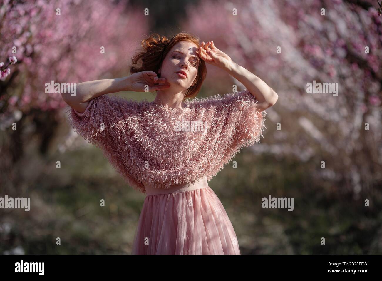 Beautiful young girl with red hair in a gentle peach garden, which blossomed. The concept and idea of skin and hair care. Stock Photo