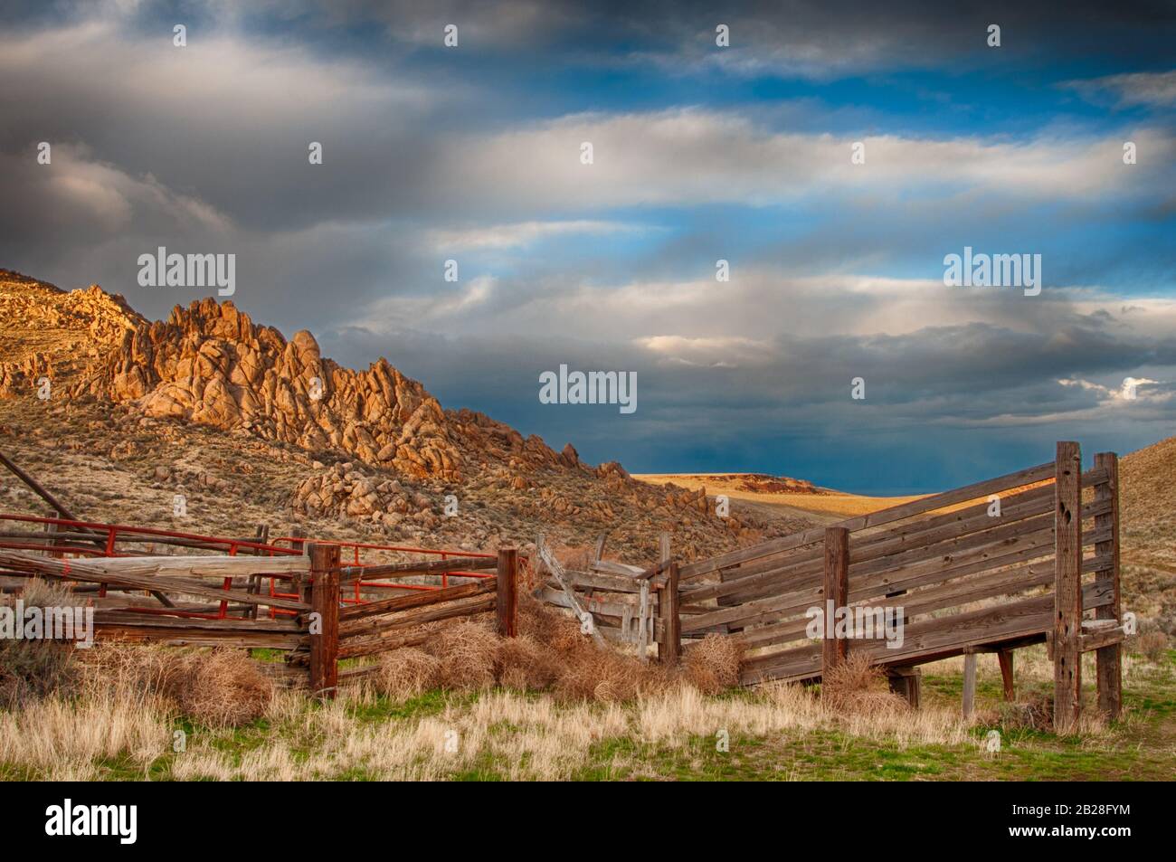 Wooden cattle loading ramp sits on the shady side of the hills with the setting sunlight illuminating the higher Owyhee County Idaho rocky hilltops an Stock Photo