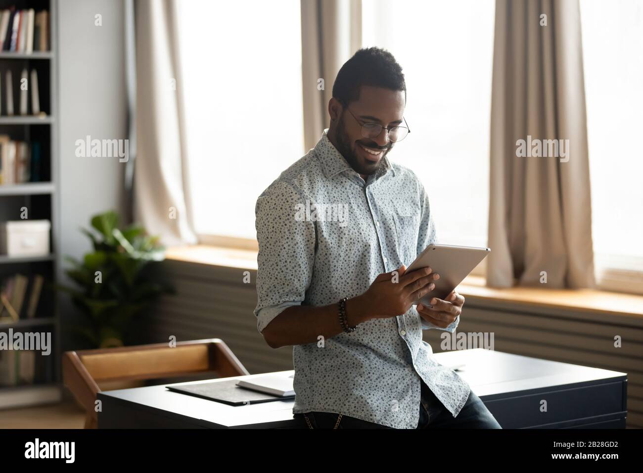 Smiling businessman web surfing information at home on digital tablet. Stock Photo