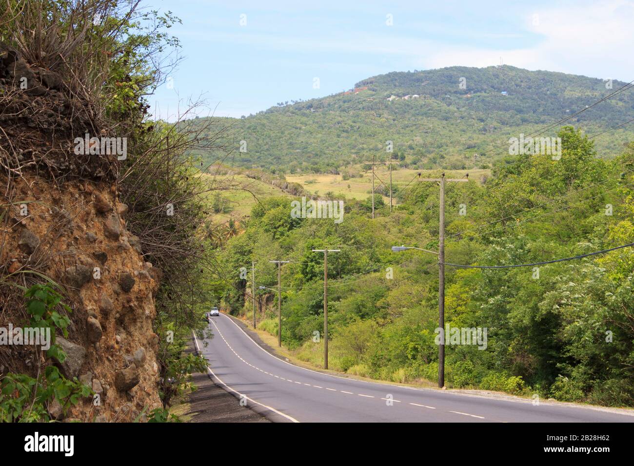 Surreal, Canelles, asphalt road with white markings on the way to Vieux Fort, on a summer day greenery everywhere trees, rocks an electric pole lines Stock Photo