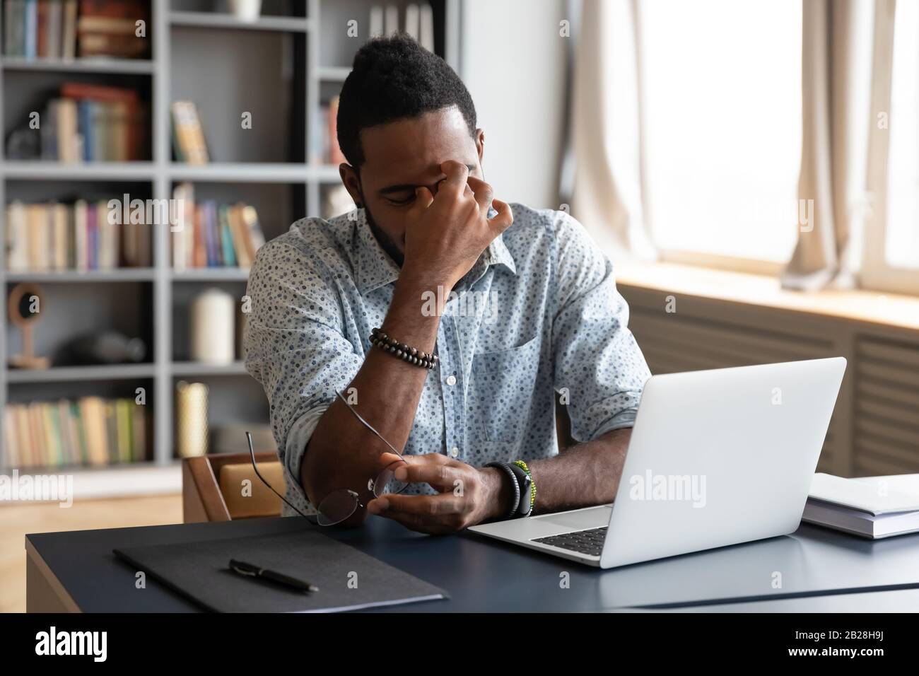 Frustrated young biracial guy taking off eyeglasses, massaging nose bridge. Stock Photo