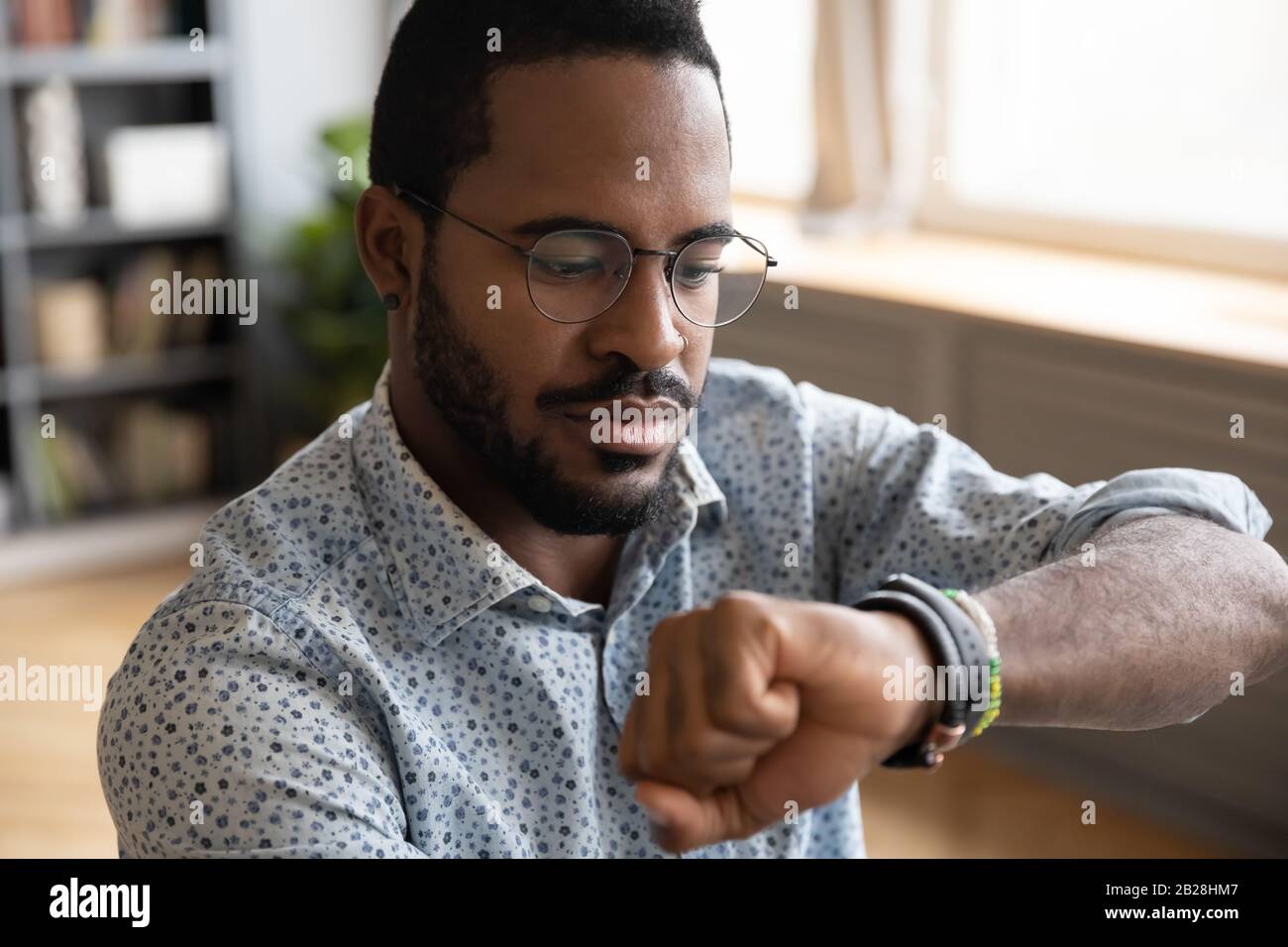 Focused young african ethnic businessman checking time on wristwatch ...