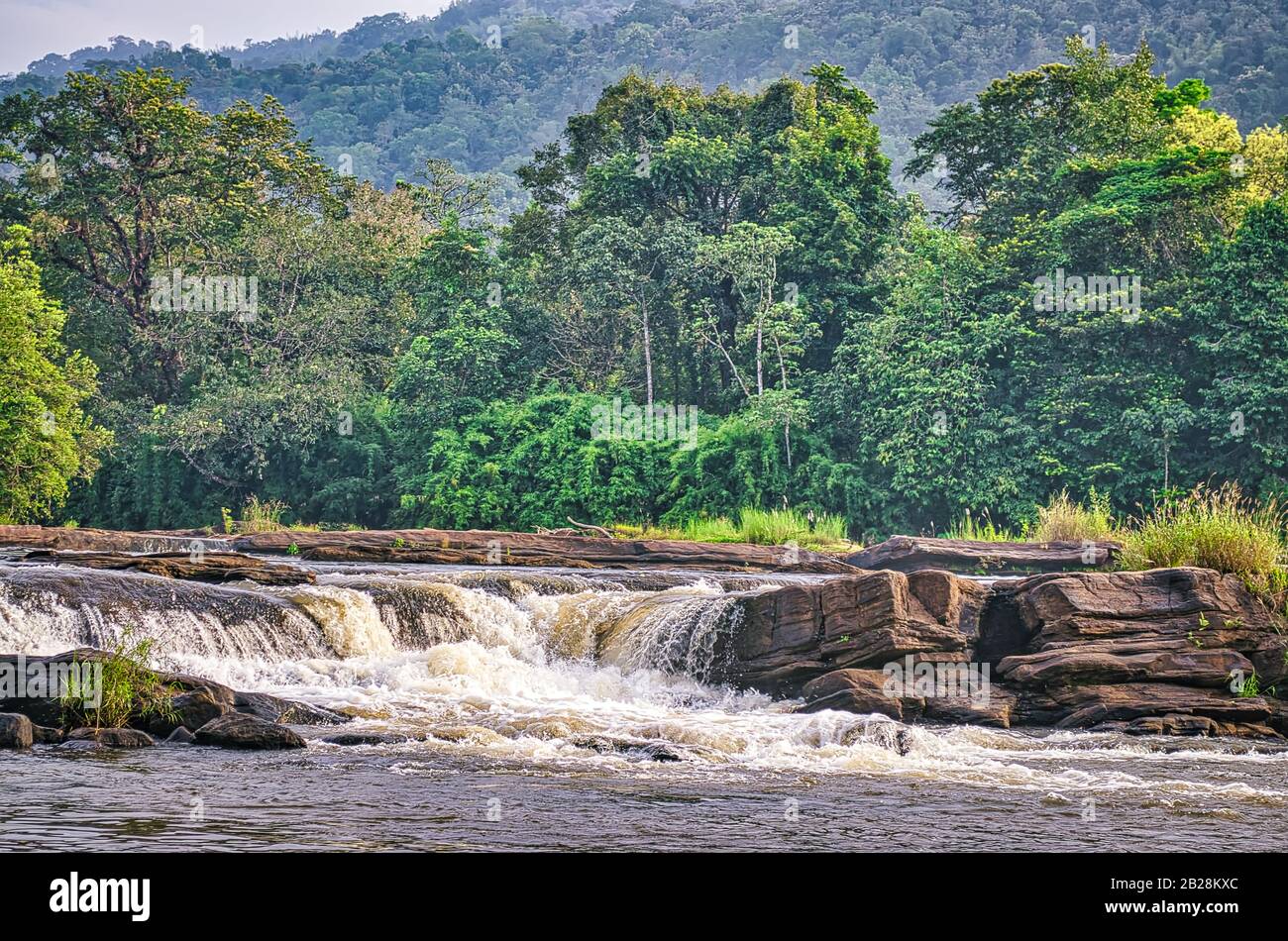 Waterfall through rocks in a river banked by thick green vegetation in Kerala, India. Stock Photo