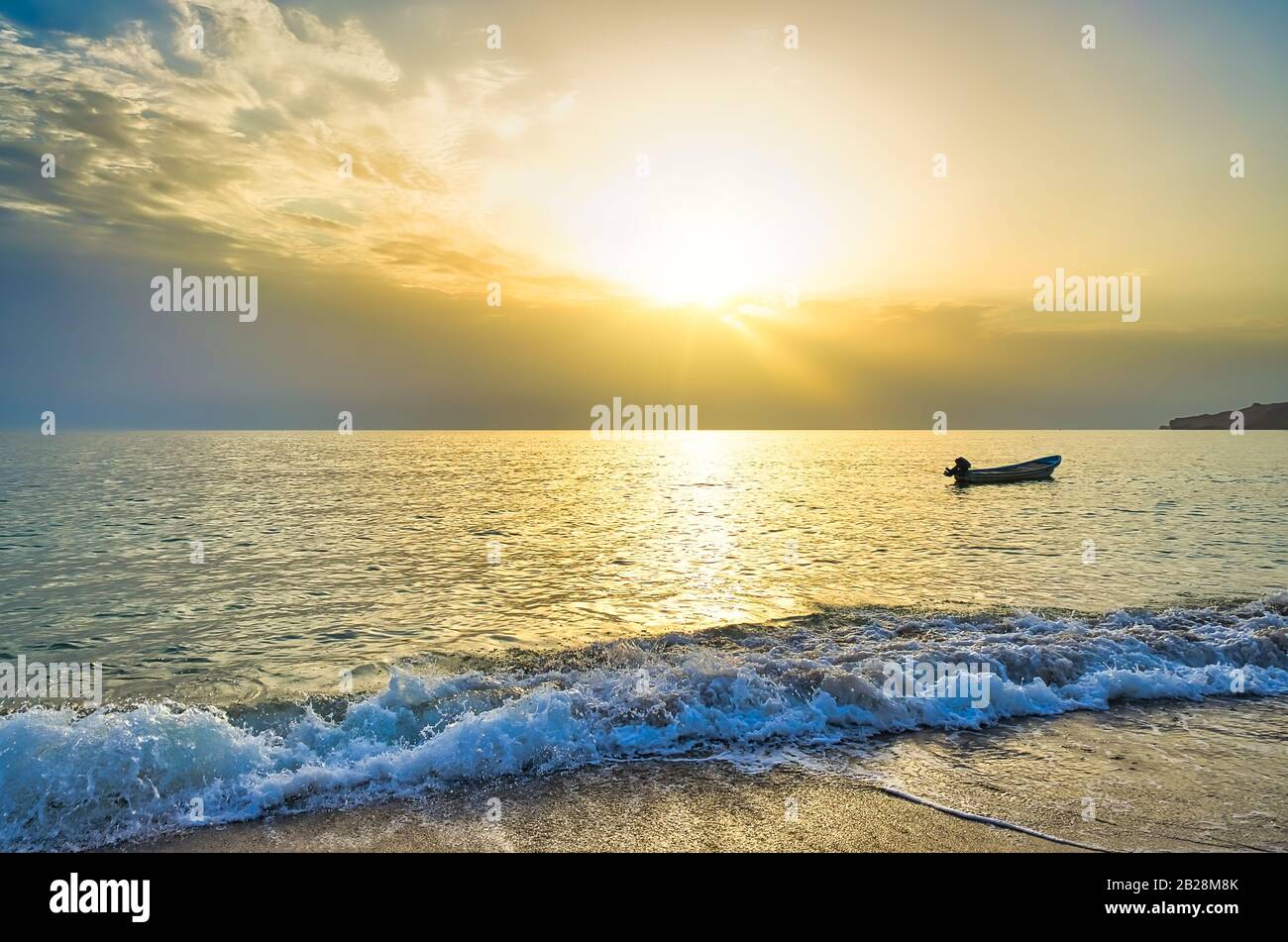 Empty fishing boat welcoming morning sunlight on the beach. Waves Splashing in the Golden Hour. From Muscat, Oman. Stock Photo