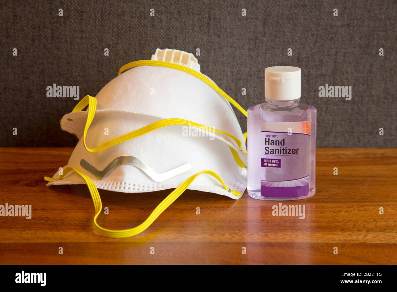 Hand sanitizer and pair of face masks on home table with gray fabric background reflect personal protection supplies to guard against coronavirus pand Stock Photo