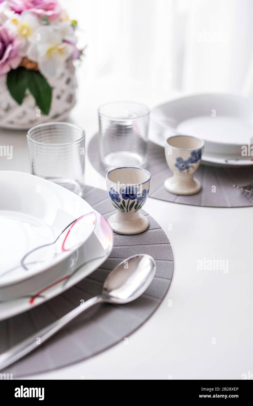 Minimalist white tableware on a white surface dining table in natural light, angled view. Stock Photo
