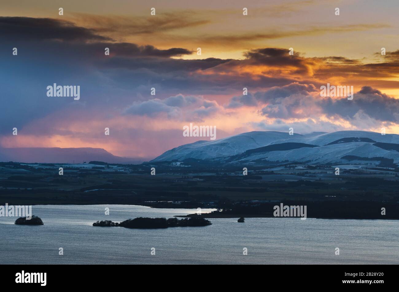 Winter sunset over Loch Leven and the Ochil hills, with Stirling and the Wallace monument in the distance. Stock Photo